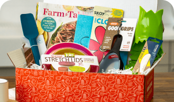 Gift box with kitchen gadgets, magazine, and utensils on a table.