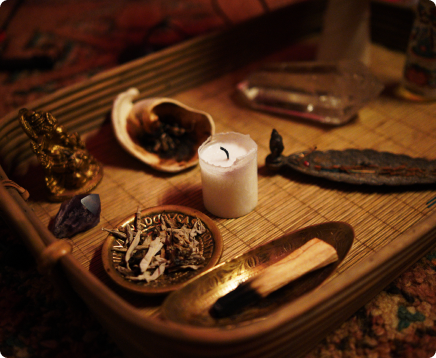 Spiritual altar with candle, sage, crystals, and small statue on a wooden tray.