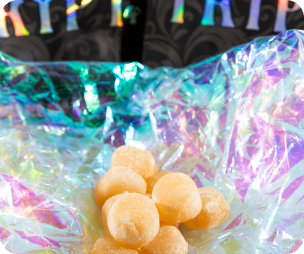 Yellow gum balls on a shiny, iridescent surface with a dark, colorful background.