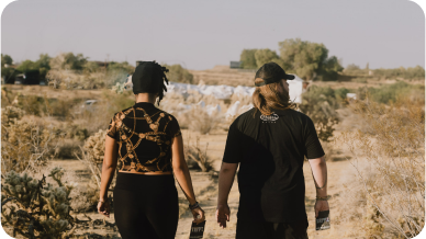 Two people walking in a desert landscape holding pamphlets.