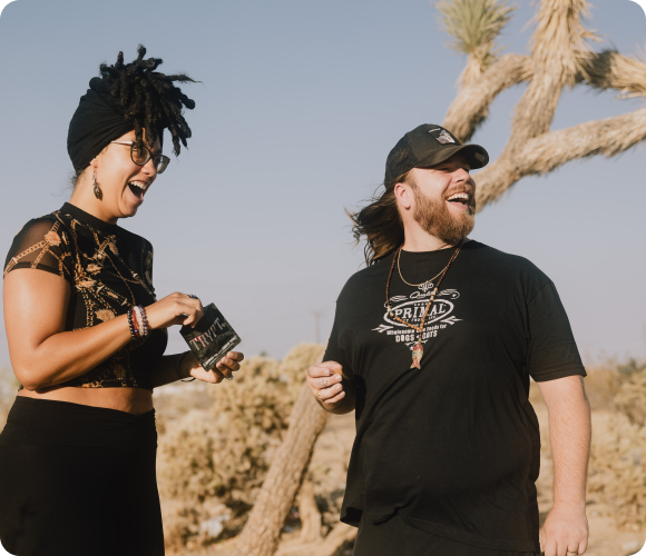 Two people laughing together outdoors with desert scenery in the background.