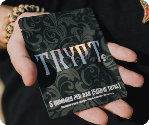 Hand holding a package labeled 'TRIPT' containing 5 gummies for a total of 500mg.