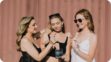 Three women enjoying themselves outdoors, with one holding a pack labeled 'THRIVE.'