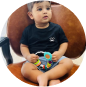 A toddler in a black shirt and shorts holding a colorful toy while sitting on a chair.