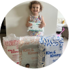 A child holding a pack of diapers, surrounded by large diaper packages.