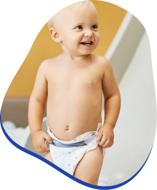 A smiling baby in a diaper standing indoors.