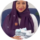Woman in purple hijab holding packages and smiling.