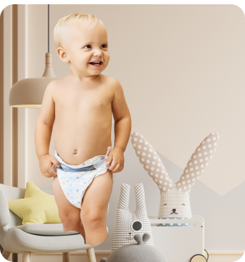 A smiling baby wearing a diaper stands in a cozy, modern nursery.