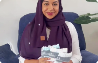 A woman in a purple hijab holding a bundle of patterned fabrics.