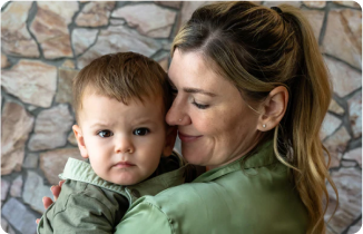A woman lovingly holds a baby in front of a stone wall.
