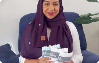 Woman in a hijab holding newborn baby diapers, sitting on a chair.