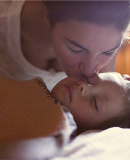 A woman kisses a sleeping child on the forehead.