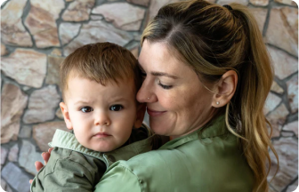 Mother holding her serious-faced child in front of a stone wall background.