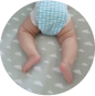 Baby wearing a blue diaper lying on a grey blanket with white clouds.