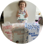 A smiling child holding a pack of diapers with three larger diaper packages on the floor.