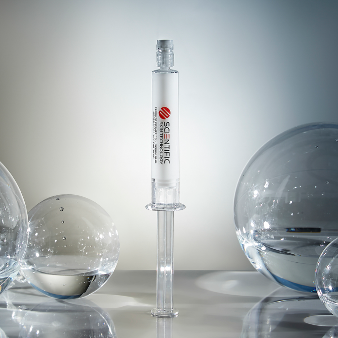 A glass syringe surrounded by clear, spherical objects on a reflective surface.