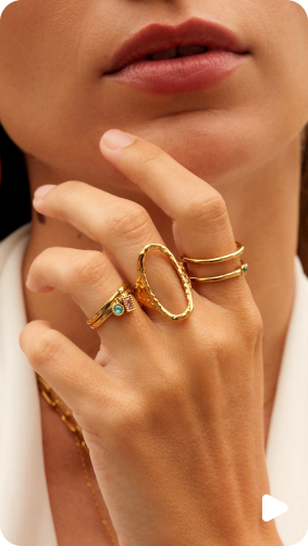 Person wearing multiple gold rings on their fingers, with a close-up focus on the hand.