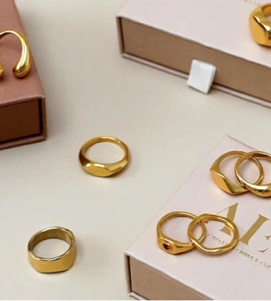 Gold rings and jewelry are displayed on boxes on a light-colored surface.