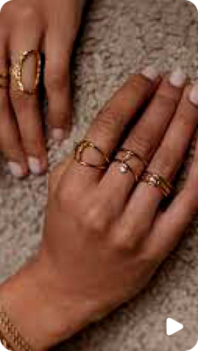 Two hands adorned with multiple gold rings against a textured background.