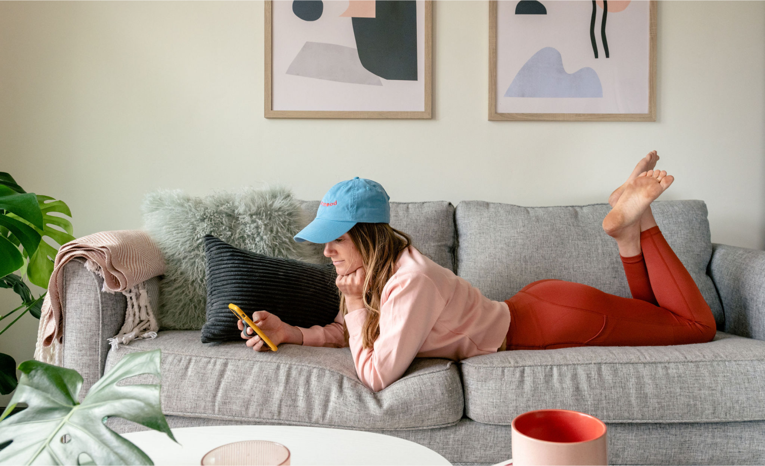 Woman in casual clothes lying on a sofa using a smartphone.