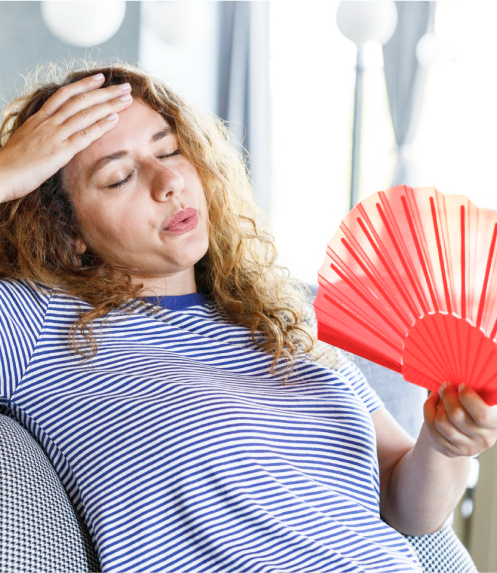 Person fanning themselves and looking overheated while seated indoors.