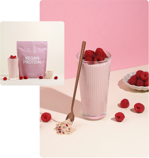 Pink vegan protein shake with raspberries and spoon on pastel background.