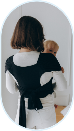 A woman with short hair wears a baby in a black wrap carrier.