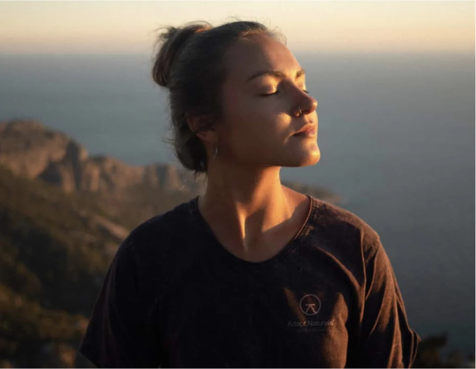 Person enjoying the sunlight on a scenic cliff with ocean view.