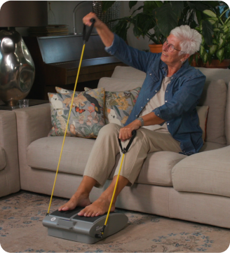 Older adult using a seated exercise device with resistance bands on a couch.