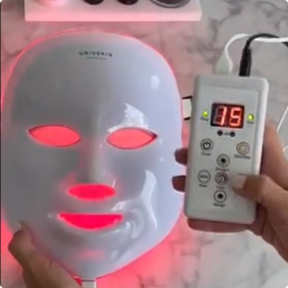 LED facial mask with remote, glowing red.