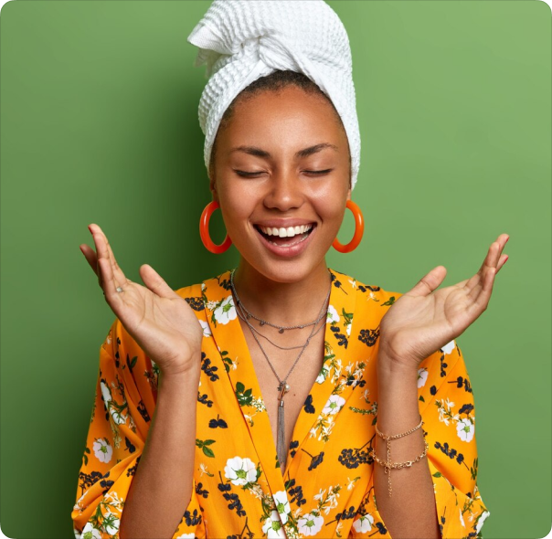 Smiling person in floral robe and towel turban against green background.