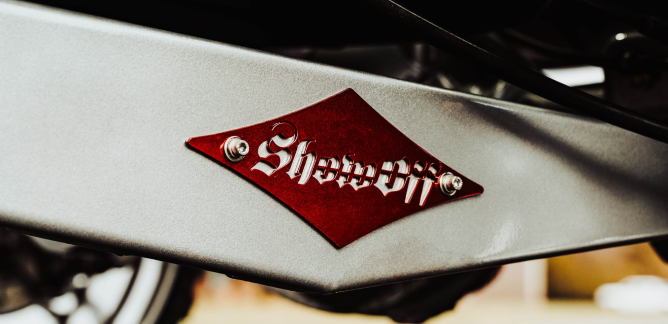 Close-up of a red diamond-shaped metal badge with 'Showoff' text on a gray surface.