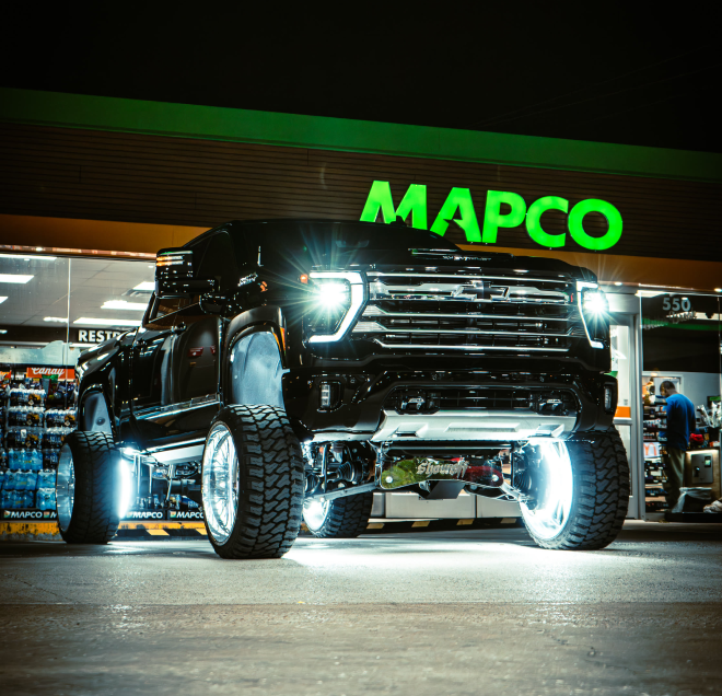 A black pickup truck with bright lights in front of a MAPCO store at night.