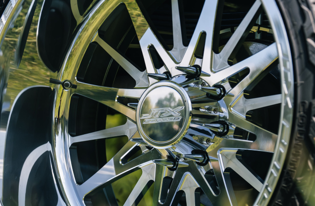 Close-up of a shiny chrome JTX aftermarket car wheel and lug nuts.