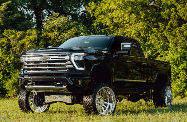 Lifted black pickup truck with large chrome wheels in a grassy area.