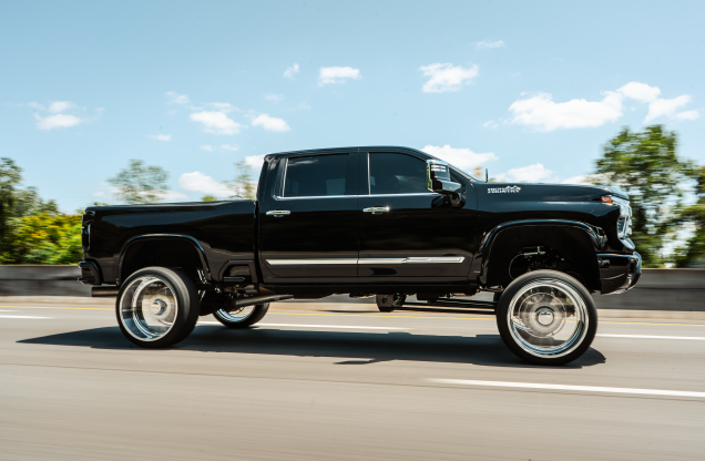 Black pickup truck with large, shiny wheels driving on a highway.