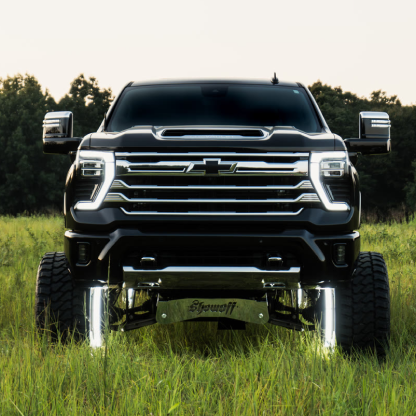 A lifted black Chevrolet pickup truck in a grassy field with trees in the background.