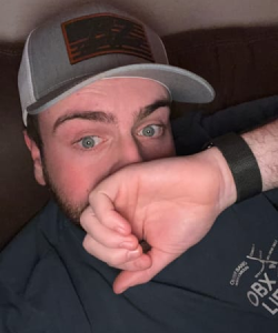 Person wearing a cap, covering part of their face with their hand.