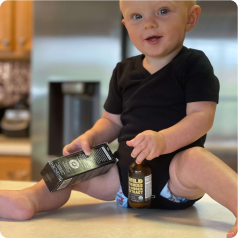 A baby sitting on a kitchen counter holding two bottles, smiling.